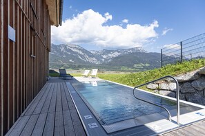 En træterrasse med pool, liggestole og udsigt til et bjerg.