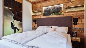 Ein Schlafzimmer mit Holzbalkendecke, einem Bett mit weißer Bettwäsche, zwei Nachttischen mit Lampen und einem gerahmten Bild von einer Berglandschaft.