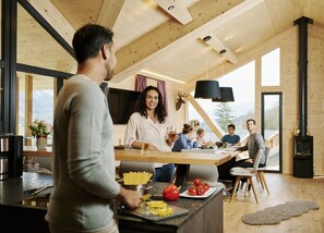 Et moderne køkken med en central ø, træbjælker og et stort vindue med udsigt til et bjergrigt landskab.