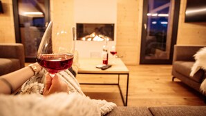 A cozy living room with a fireplace, a sofa, and a glass of red wine.