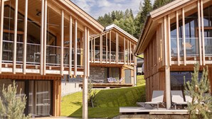A wooden cabin with large windows, a balcony, and a deck with lounge chairs.