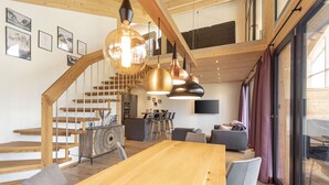 A modern interior with a wooden staircase, a dining area, and a living space with a TV and artwork on the walls. - Premium Apartment gallery with 3 bedrooms and sauna & whirlpool (Haus im Ennstal)