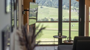 A modern living room with a large window offering a view of a green landscape and mountains. - Premium Apartment gallery with 3 bedrooms and sauna & whirlpool (Haus im Ennstal)