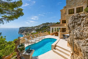 A swimming pool with a stone wall, outdoor seating, and a view of the sea. - Llamp Sea View, Villa 5StarsHome Mallorca (Port d' Andratx)
