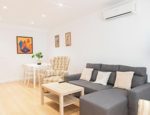 A modern living room with a grey sofa, a wooden coffee table, a striped armchair, a dining table with chairs, and a potted plant.