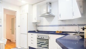 Une cuisine avec des meubles blancs, un plan de travail bleu, un four encastré et une hotte en acier inoxydable.