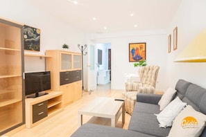 A modern living room with a sofa, TV, and a dining area with a chair.