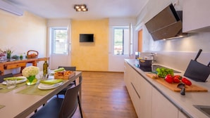A modern kitchen with a dining area, wooden flooring, and a flat-screen TV mounted on the wall. - Appartamento Bianca Gemma (Riva del Garda)