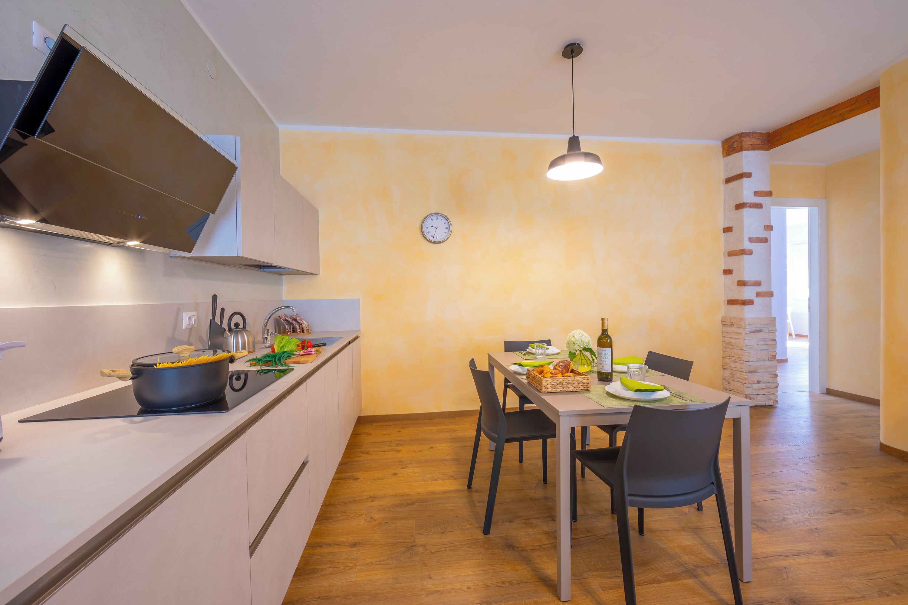 Una cocina moderna con comedor, un reloj en la pared y una escalera que lleva a otra habitación.
