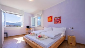 A bedroom with a large bed, a desk, a chair, and a view of the mountains through a window. - Appartamento Bianca Gemma (Riva del Garda)