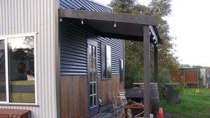 Eine Holzterrasse mit Gartenmöbeln, einem Grill und einem Mülleimer.