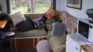 Ein gemütliches Zimmer mit einem grünen Sofa, bunten Kissen, einem kleinen Hocker und einer Mikrowelle.
