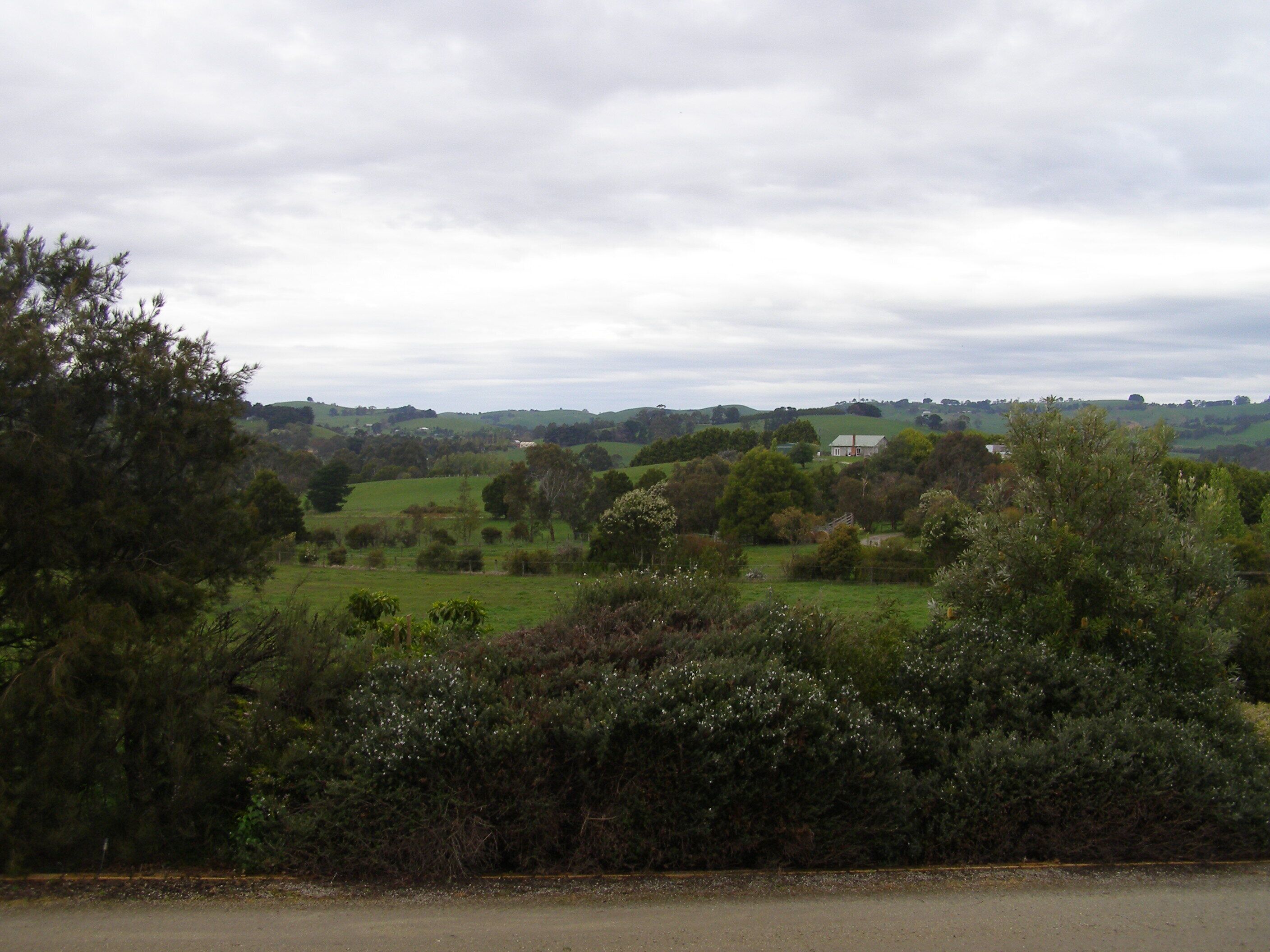Un paysage rural caractérisé par des collines douces, une maison et une végétation luxuriante.