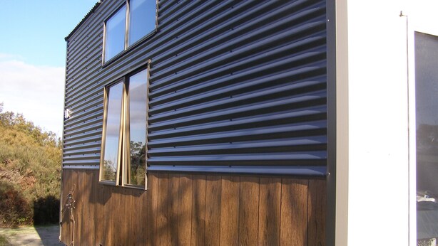 Ein Wohnmobil mit Holzaußenverkleidung und Metallverkleidung, mit einem großen Fenster und einer sichtbaren Tür.