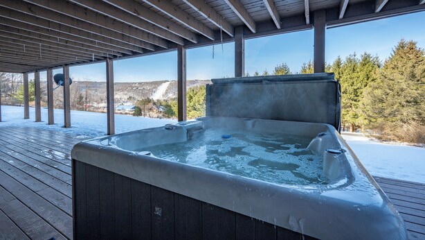 A hot tub under a wooden pergola with a snowy landscape in the background.