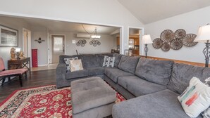 A spacious living room with a grey sectional sofa, a red patterned rug, and a dining area with a red chair and table.