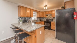 A kitchen with wooden cabinets, a granite countertop, a black refrigerator, and a stainless steel range hood.