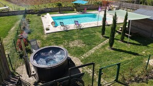 En pool med solstolar, ett bubbelbad och en inhägnad trädgårdsdel.