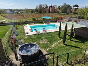 A swimming pool with lounge chairs, a hot tub, and a fenced garden area. - Charming Village House with Shared Heated Pool, Near Attractions, and Private Garden (Le Menoux)