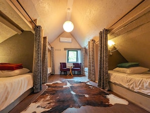 A narrow room with two beds, a table, and a cowhide rug. - Charming Village House with Shared Heated Pool, Near Attractions, and Private Garden (Le Menoux)