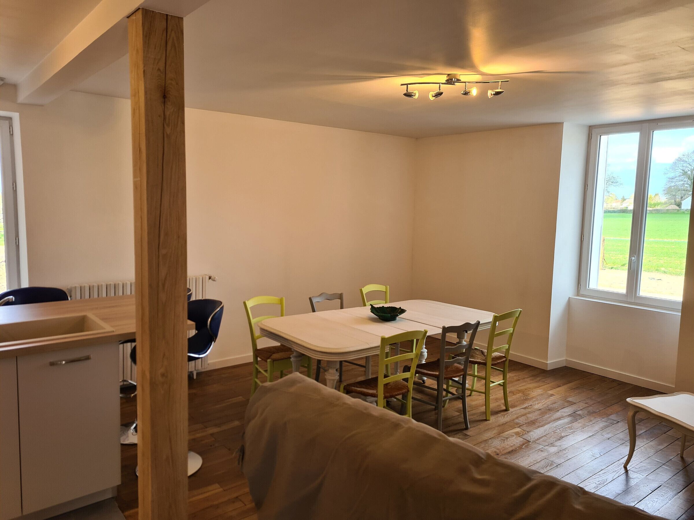 A dining area with a table and chairs, a window with a view of greenery, and a wooden floor.