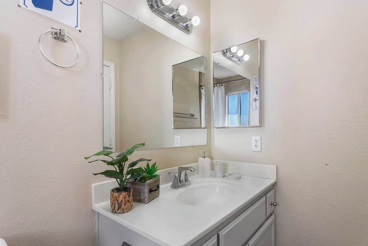 Une salle de bain avec un lavabo blanc, deux miroirs, un porte-serviettes et une plante en pot.