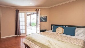 A bedroom with a bed, a nightstand, a painting, and a door leading to an outdoor area. - Rare 4BR Beauty with Pool 7 min to Strip! (Las Vegas)