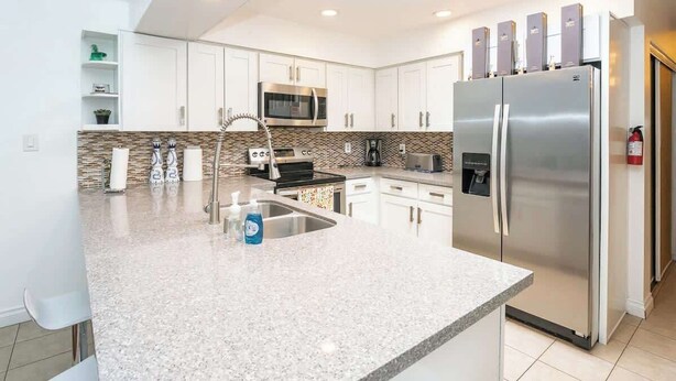 A modern kitchen with white cabinets, a stainless steel refrigerator, a microwave, and a granite countertop. - Rare 4BR Beauty with Pool 7 min to Strip! (Las Vegas)