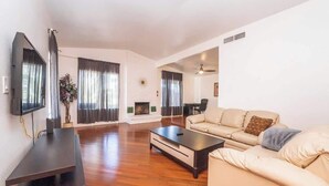 A spacious living room with a flat-screen TV, a fireplace, a sofa, and a coffee table. - Rare 4BR Beauty with Pool 7 min to Strip! (Las Vegas)