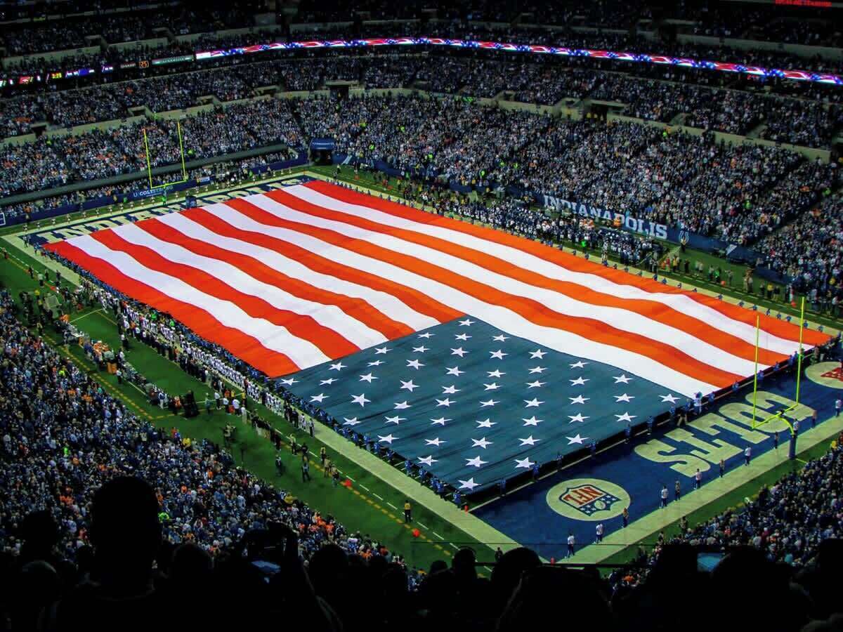 A stadium with a large American flag covering the field.