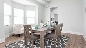 A dining area with a wooden table, four chairs, and a chandelier. There are large windows and a view of the outside. - Brand New! Two Indy Homes Perfect for Groups! (Indianapolis)