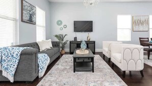 A living room with a grey sofa, a white armchair, a coffee table, and a TV on the wall. - Brand New! Two Indy Homes Perfect for Groups! (Indianapolis)