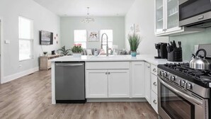 A modern kitchen with white cabinetry, a stainless steel dishwasher, a gas stove, and a microwave. - Brand New! Two Indy Homes Perfect for Groups! (Indianapolis)