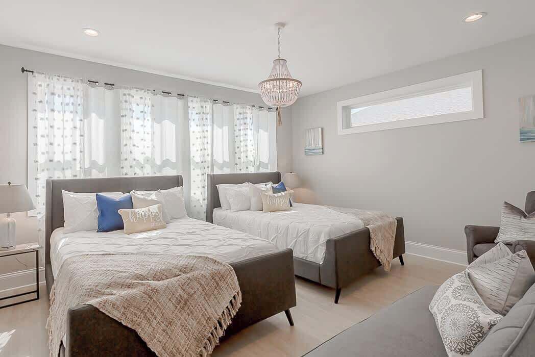 A modern bedroom with two beds, a chandelier, and a large window.