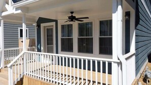 A covered porch with a ceiling fan, white railings, and a wooden deck.
