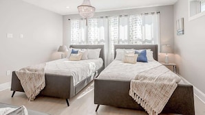A modern bedroom with two beds, a chandelier, and a window with curtains.