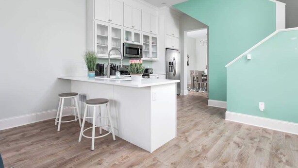 Een moderne keuken met witte kasten, een centraal eiland met krukken, en een wand in teal blauw.