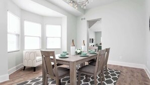 Een eetgedeelte met een houten tafel, vier stoelen en een kroonluchter. Aan de linkerkant bevinden zich grote ramen.