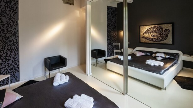 Ein modernes Schlafzimmer mit einem großen Bett, einer Glastrennwand, einer schwarz-weißen Wand mit Muster und einem gerahmten Kunstwerk.