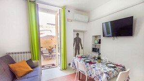 A living room with a sofa, a dining table set for two, and a TV mounted on the wall. - Casa Chiara in centro con corte privata (San Benedetto del Tronto)