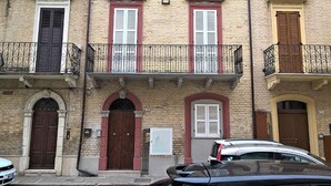A multi-story building with a brick facade, featuring balconies with wrought iron railings, arched doorways, and a mix of red and white window shutters. - Casa Chiara in centro con corte privata (San Benedetto del Tronto)