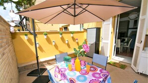An outdoor patio with a table, chairs, and a large umbrella. There are potted plants on the wall and a door leading to an interior space. - Casa Chiara in centro con corte privata (San Benedetto del Tronto)