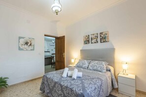 A bedroom with a bed, two bedside tables, a nightstand, a door, and a ceiling light.