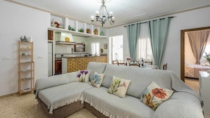 Ein gemütliches Wohnzimmer mit einer Couch, einem Holzregal, einer Küchenzeile und einem Esstisch für zwei Personen.
