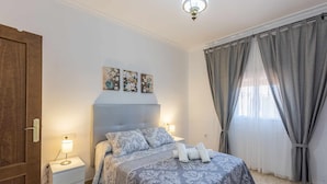 Ein Schlafzimmer mit Bett, Nachttischlampen, Deckenleuchte und einem Fenster mit Vorhängen.