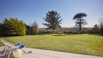 Relax on the deck with lounge chairs and a small table, overlooking a serene grassy lawn and tranquil trees.