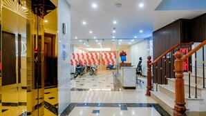Un vestíbulo de hotel con piso de mármol, un mostrador de recepción y una escalera con barandillas de madera.