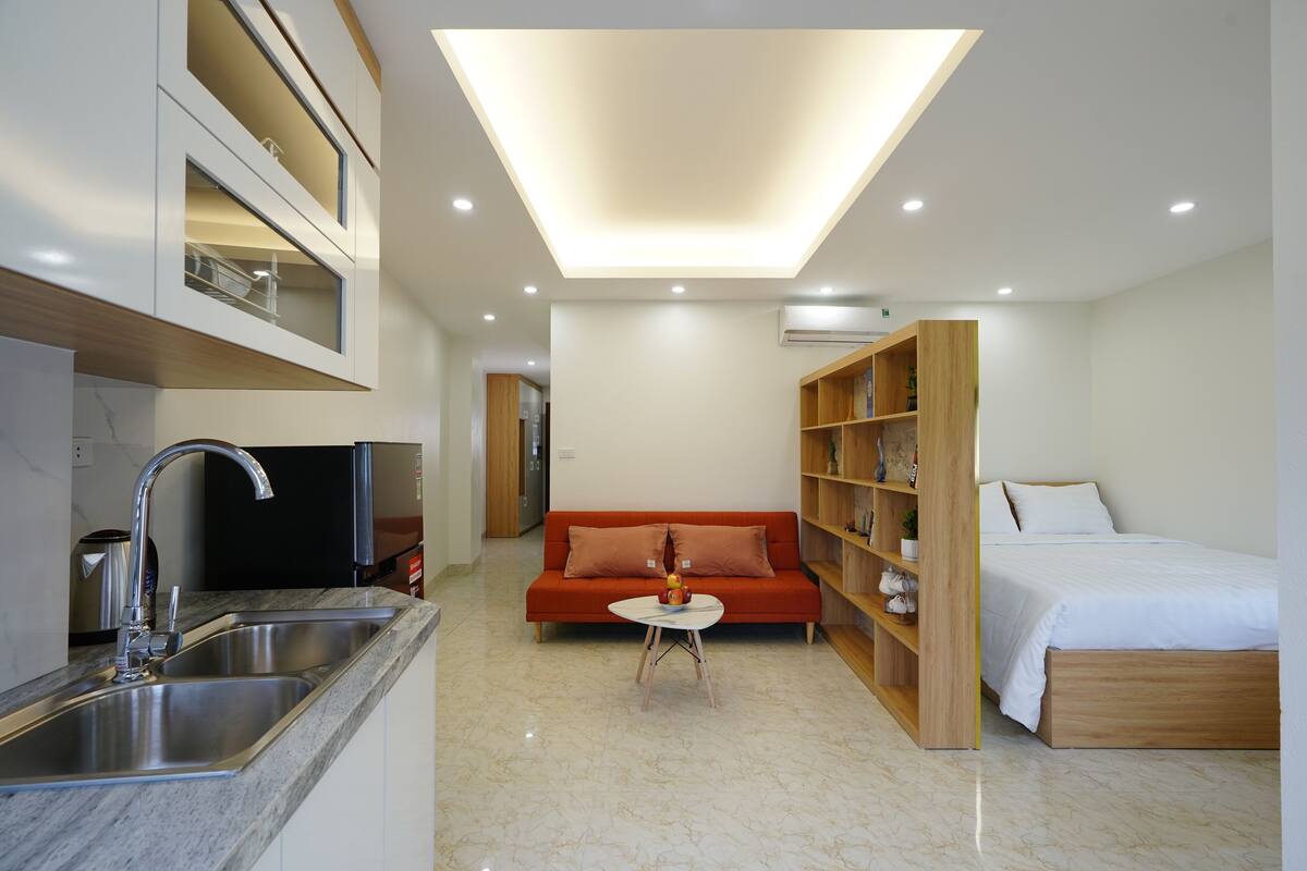 A modern hotel room with a kitchen area, a sofa, a small round table, and a bed.