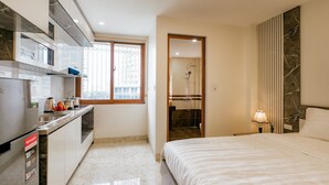 Una habitación de hotel moderna con cocina, una cama grande y un baño visible a través de una puerta abierta.