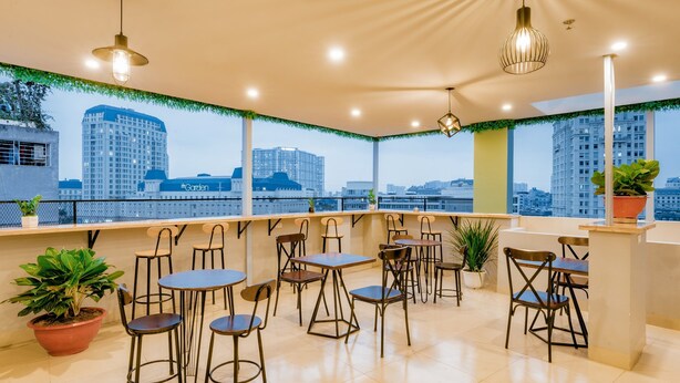 Una terraza en la azotea con varias mesas y sillas, plantas en macetas y vistas de edificios de la ciudad.